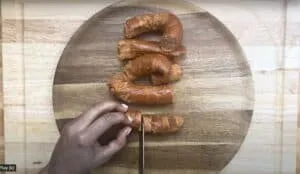 Slicing chorizo sausage on a round wooden cutting board with a knife.